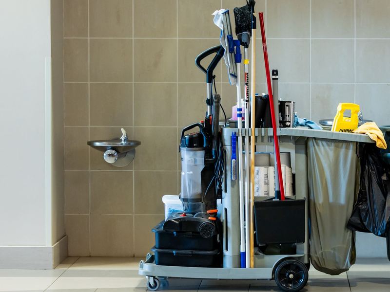 Fully stocked janitorial cart with mops, vacuum and supplies in a building corridor
