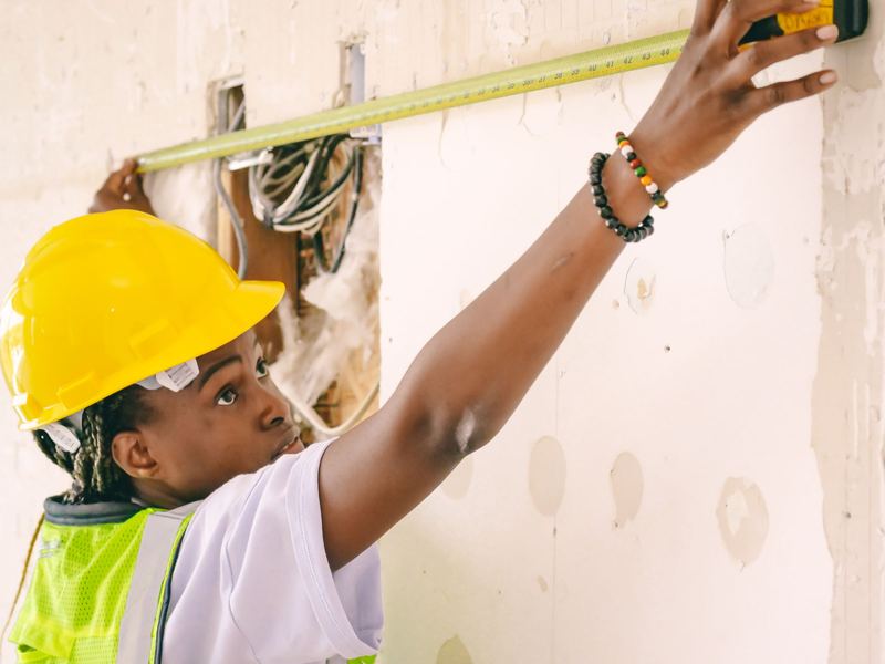 Maintenance worker in hard hat and safety vest measuring a wall for repairs
