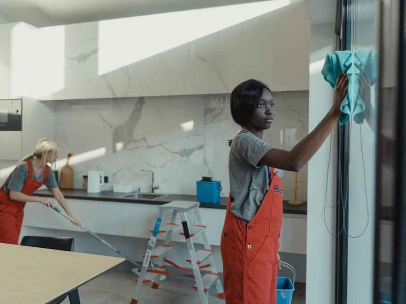 Cleaning crew wiping glass and mopping floors in a modern office kitchen
