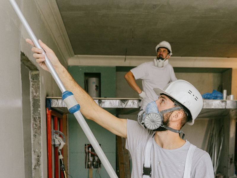 Painters in protective gear rolling fresh paint onto an interior ceiling