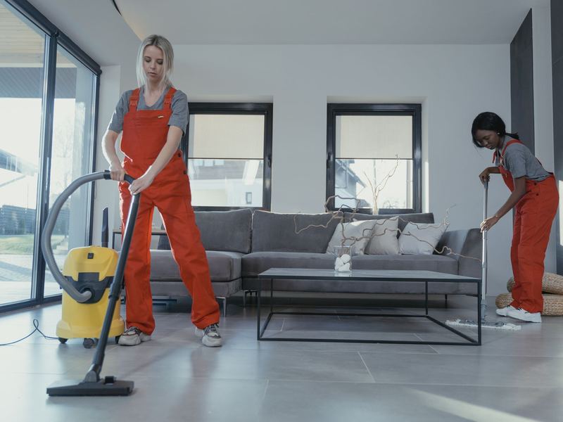 Two cleaners vacuuming and sweeping a bright modern room
